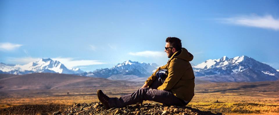 The photographer seated on a rocky rise, in profile against the snow line of the high Andes