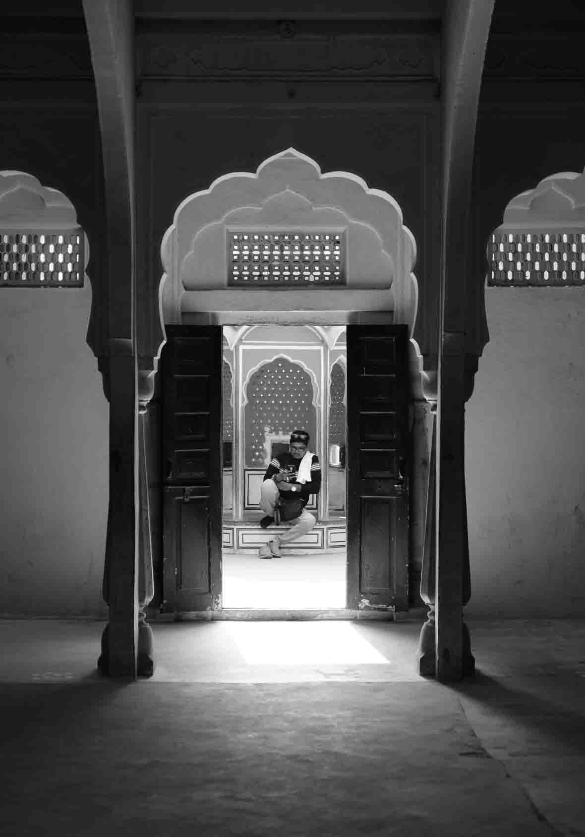 A visitor with a camera pauses on a step, framed through three receding scalloped palace arches