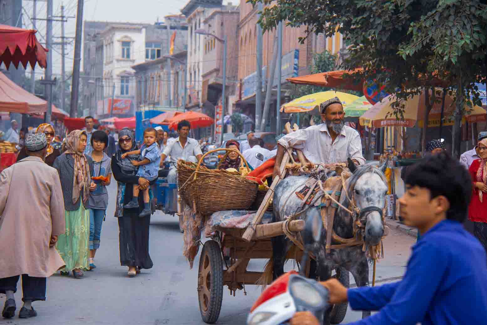 A crowded bazaar street under a run of bright parasols