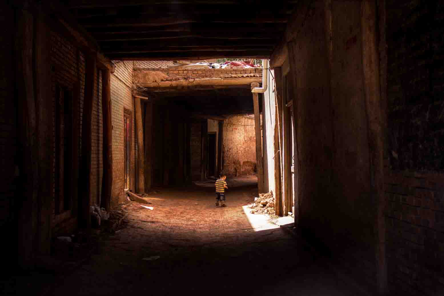 A child standing alone in a sunlit brick back alley