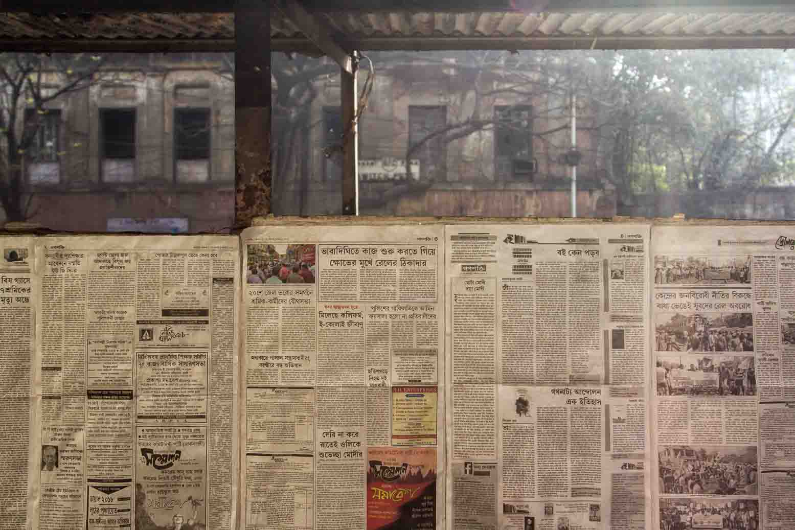 Wall papered with sheets of Bengali newspaper opposite a peeling colonial facade
