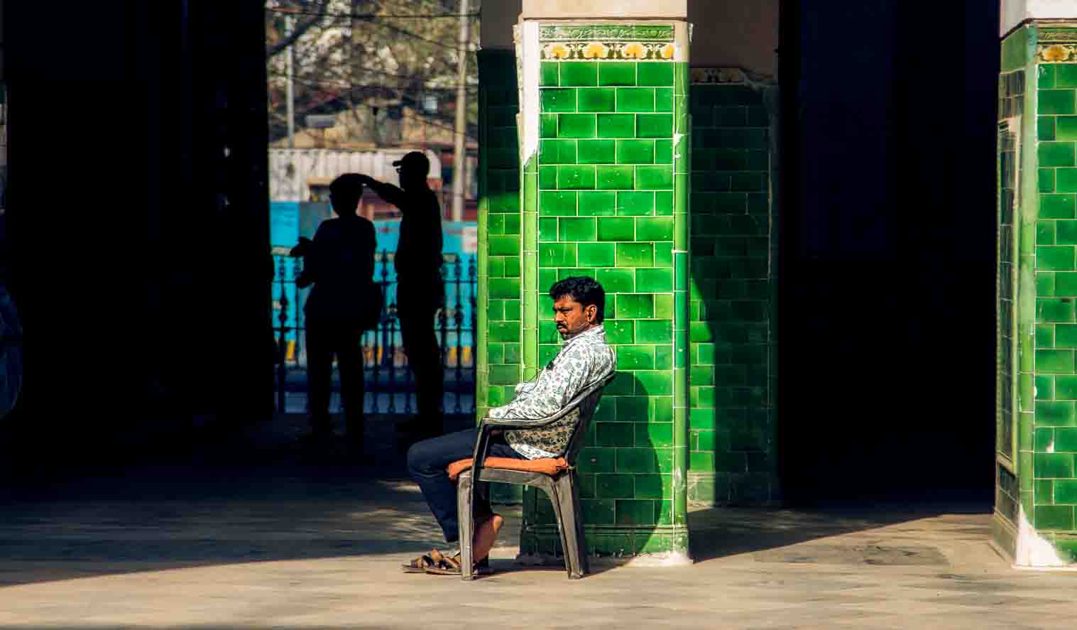 Man seated in a plastic chair against a green-tiled colonial wall
