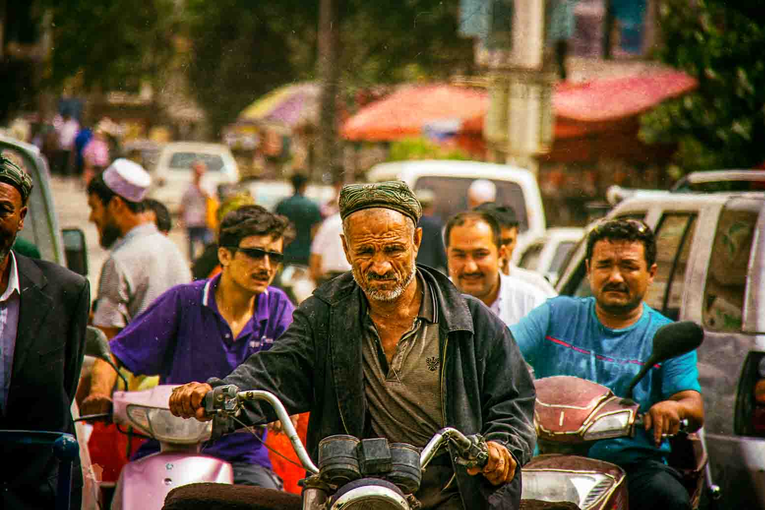 Weathered man riding a motorbike through crowded market traffic