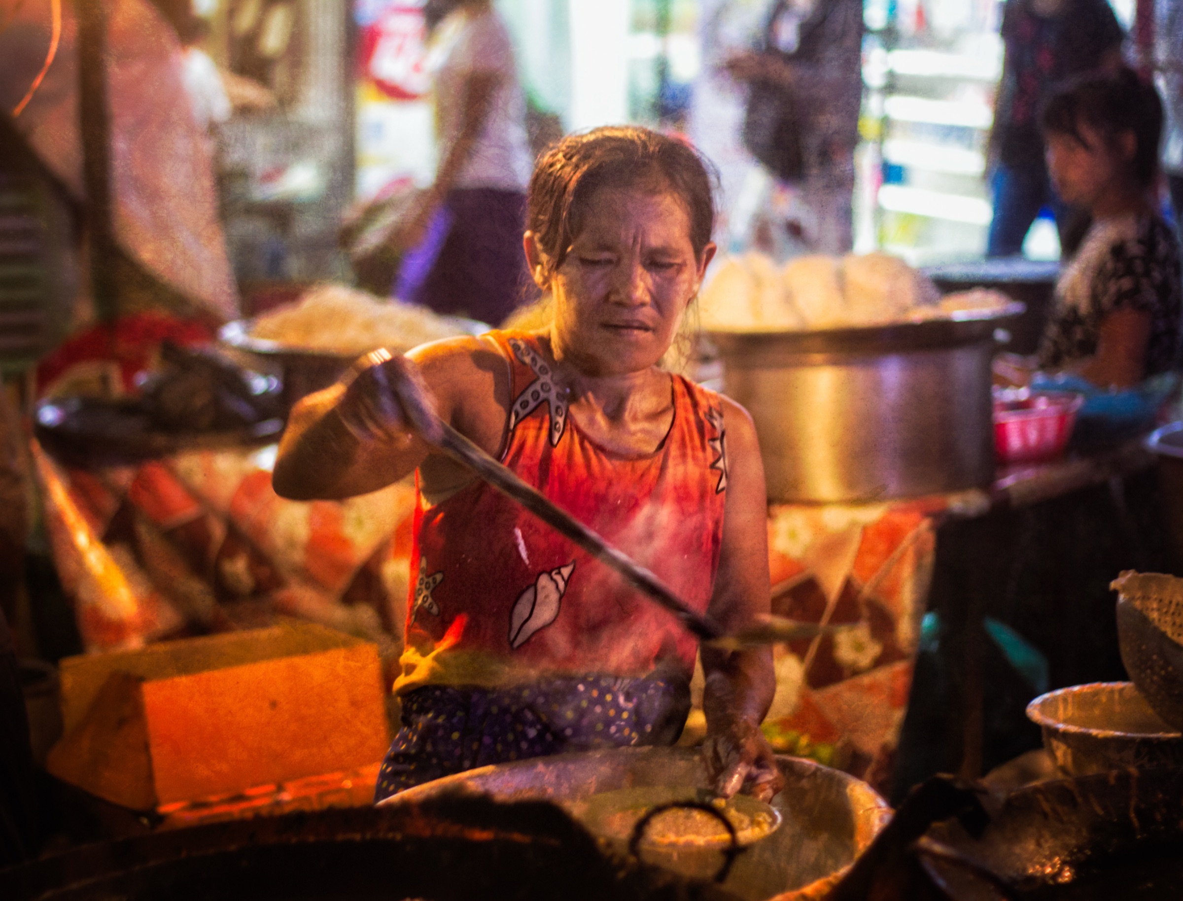 A cook at a night-market wok, lit by steam and lamplight, drawing a long ladle across the pan
