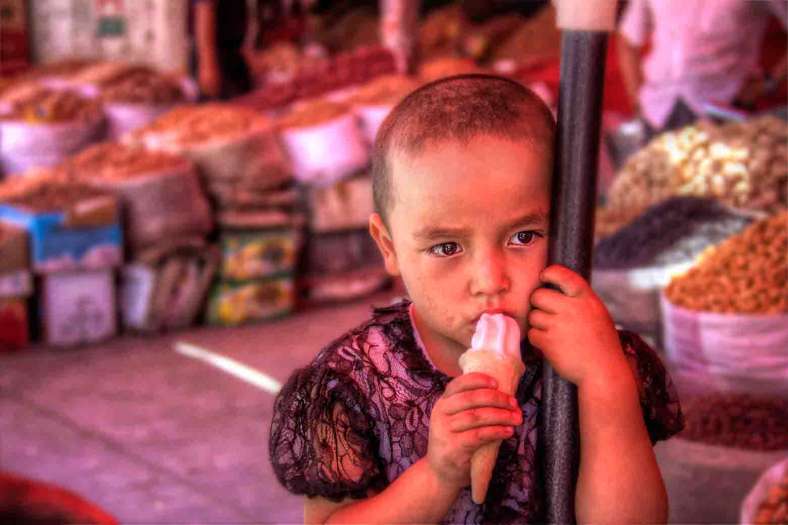 Small child in a lace dress eating an ice lolly at a dried-fruit bazaar