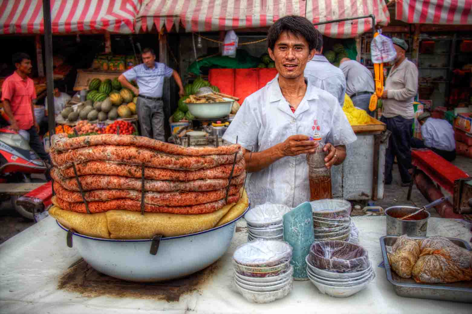 Sausage vendor smiling behind coils of merguez at a market stall