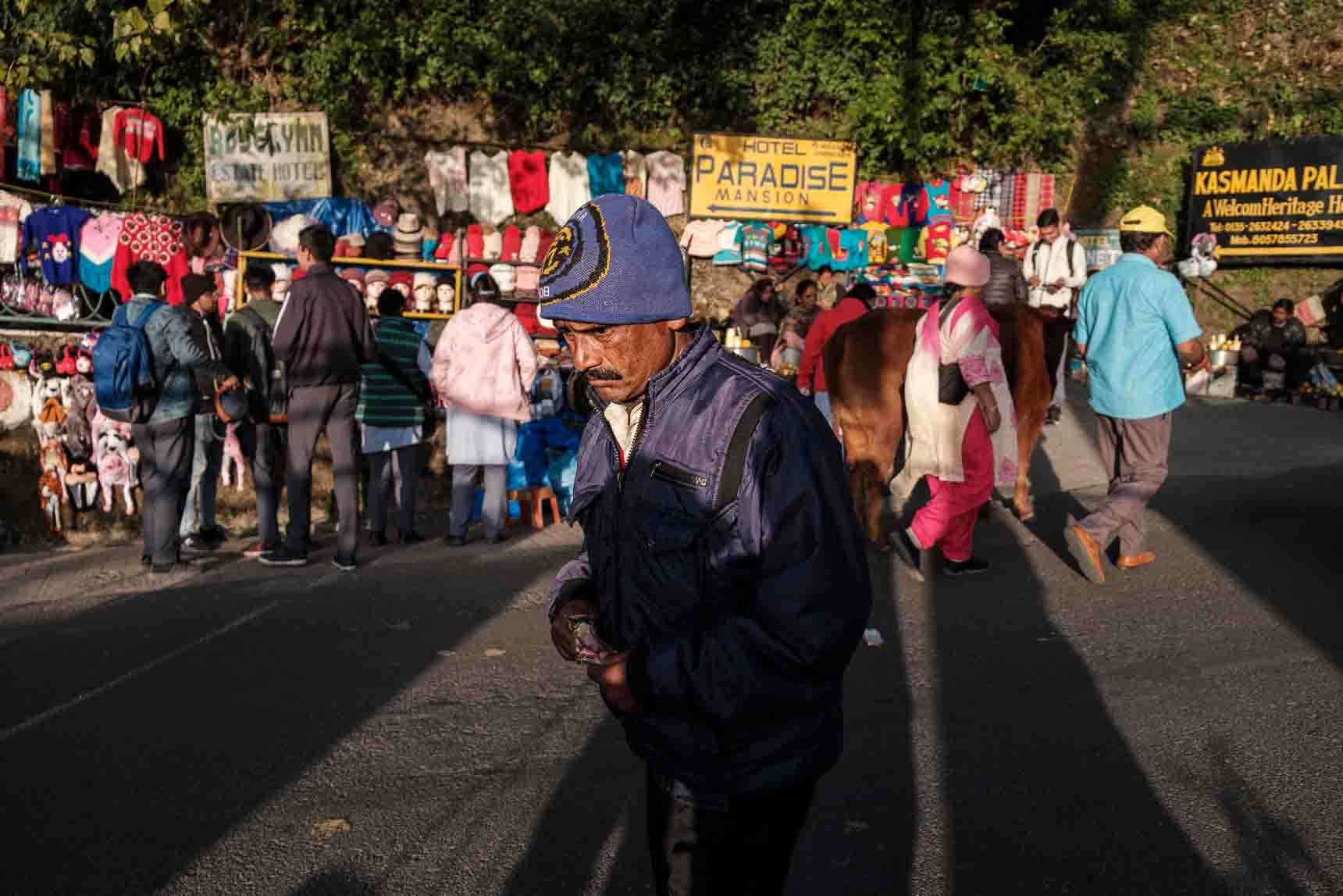 Man in a dark blue jacket and beanie walking through a hill-town market