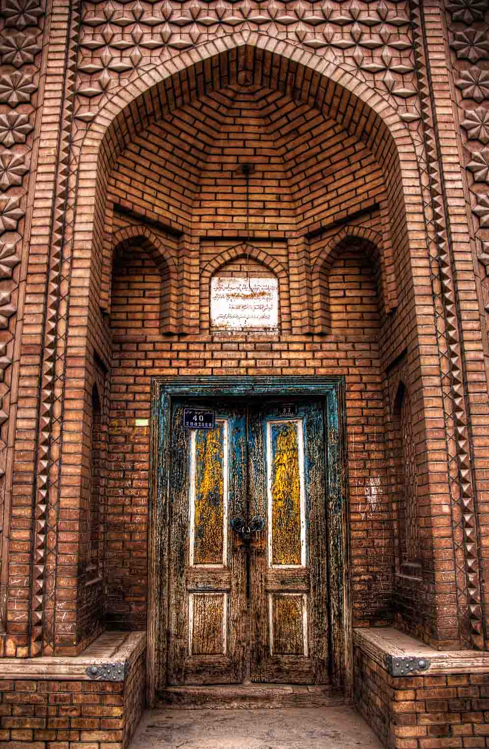 Arched brick doorway of a small mosque with carved blue-and-yellow wooden doors